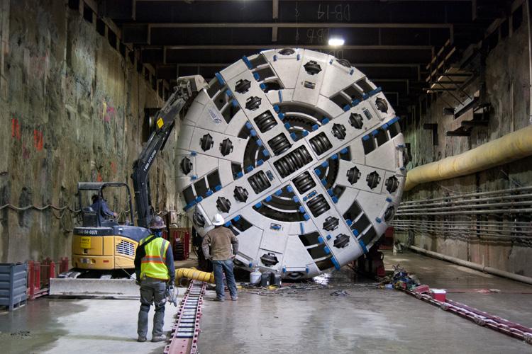 Tunnel boring machine with large circular cutter head in underground construction tunnel with workers and equipment.