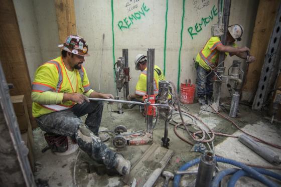 Workers in safety vests perform underground sewer line construction work in an excavated area.