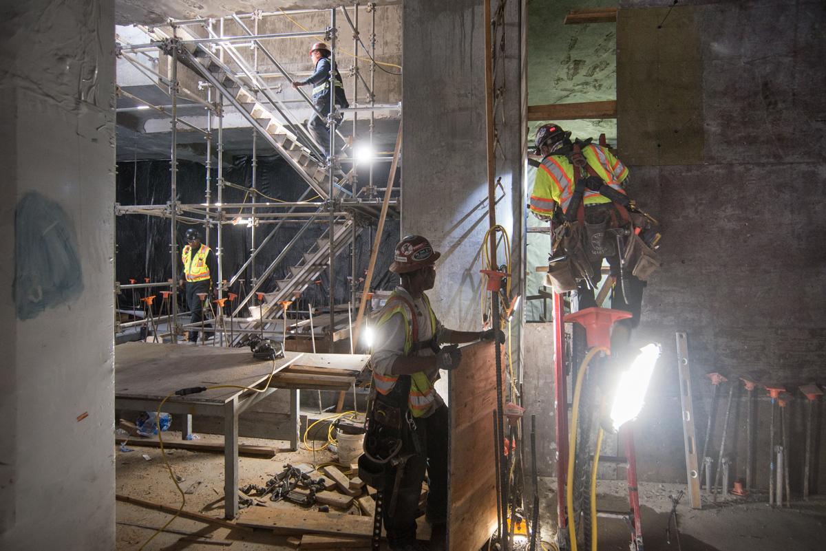 Construction workers in safety gear build concrete forms inside an underground transit station headhouse at night.
