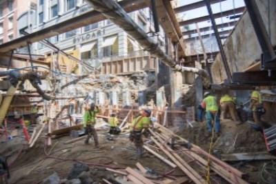 Construction workers in safety vests work on building a new concourse roof section at an urban construction site.
