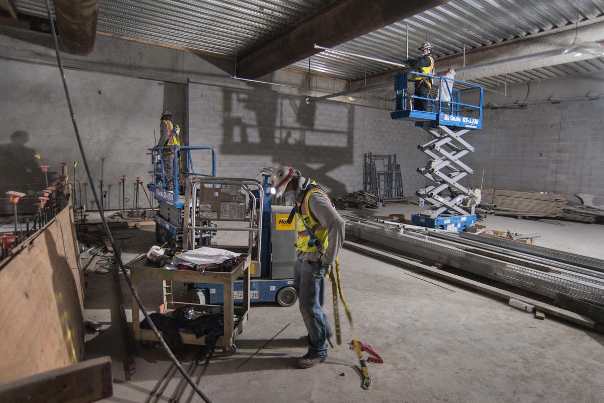Workers on scissor lifts install interior elements on a transit station mezzanine level under construction.