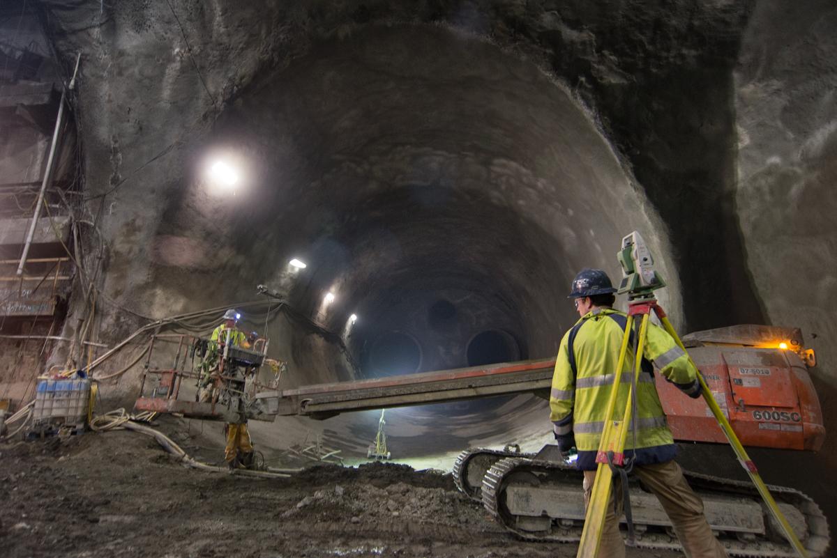 Workers in safety vests survey inside Chinatown station tunnel during construction.