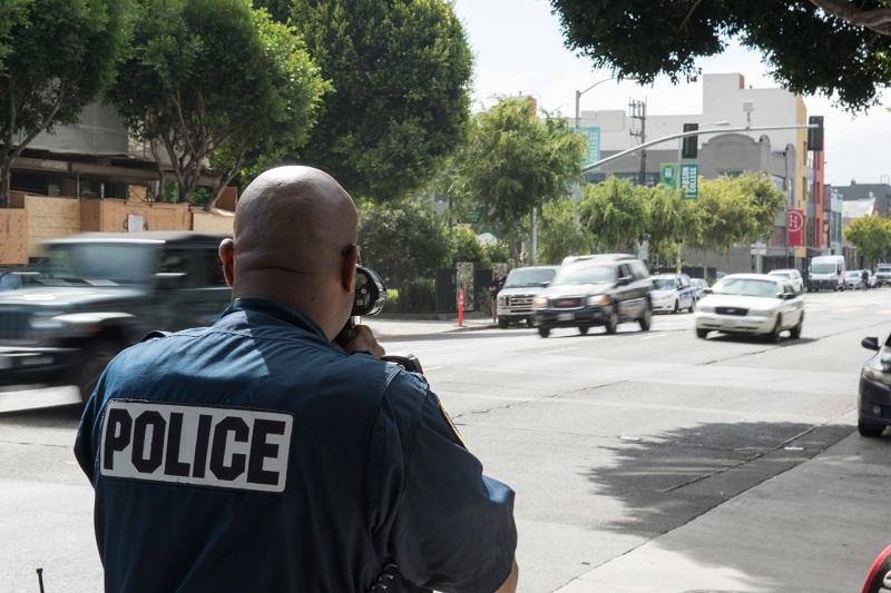 Police officer conducting speed enforcement on urban street with moving vehicles.