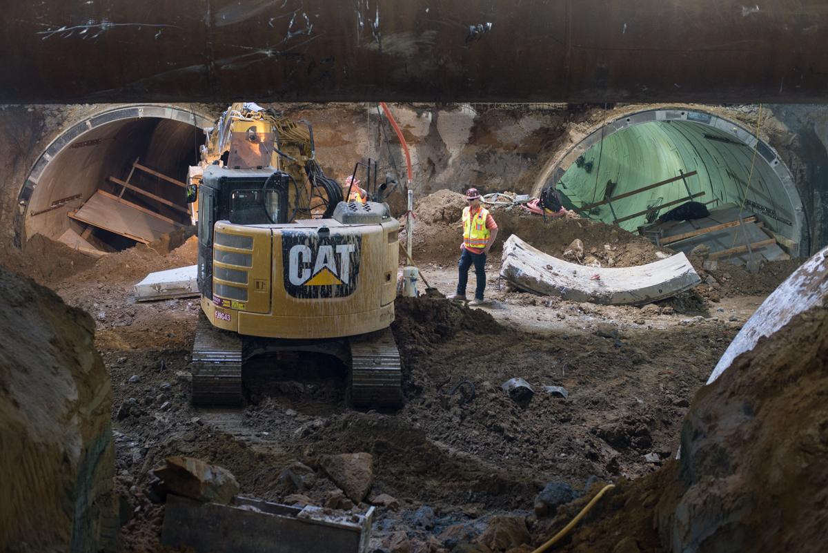 CAT excavator working in subway tunnel construction site with worker in safety vest nearby.