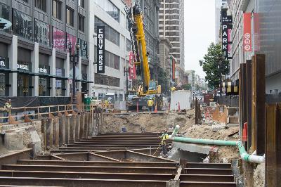 Urban construction site on Ellis Street with steel roof beams, excavation, and surrounding buildings in downtown area.