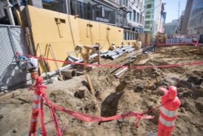 Construction site with excavation, red safety barriers, and yellow temporary structures on urban street.
