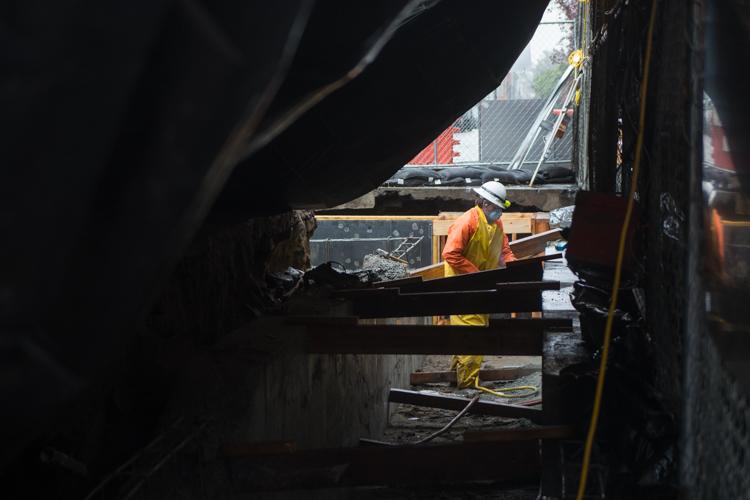 Worker in yellow safety vest using jackhammer on underground wall at construction site