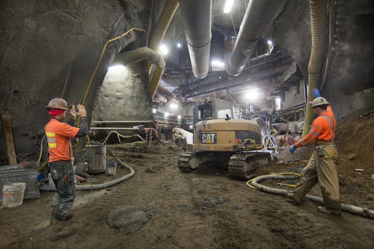 Workers in safety gear direct a CAT excavator during underground tunnel construction for the Central Subway project.