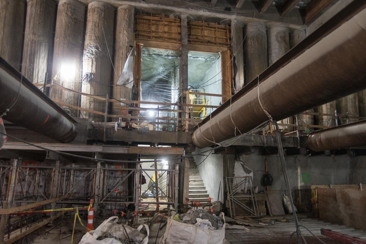 Interior construction site showing large pipes, wooden support columns, metal railings, and stairs under Stockton Street.