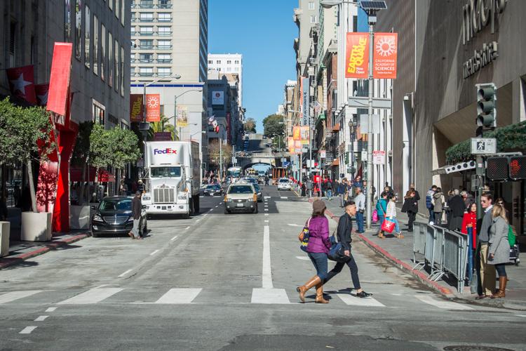 Pedestrians and vehicles on a busy urban street with holiday decorations and storefronts.