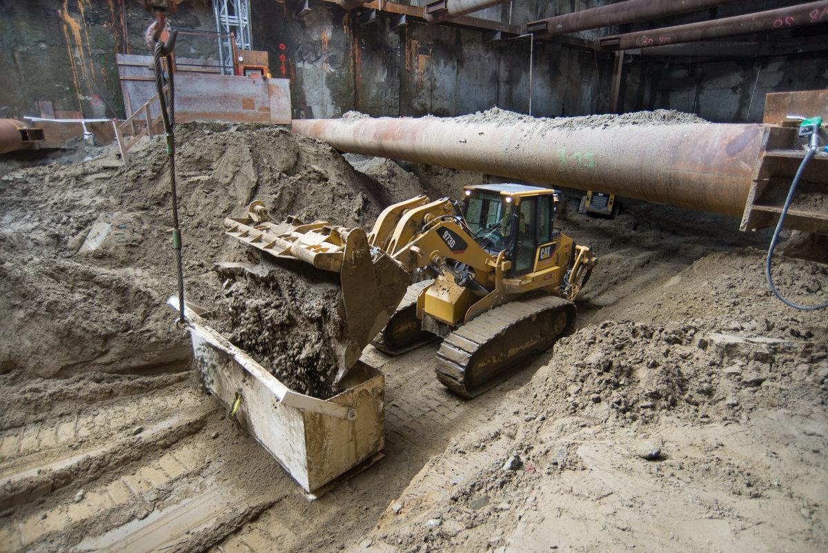 Yellow excavator loading dirt into steel box at underground construction site.