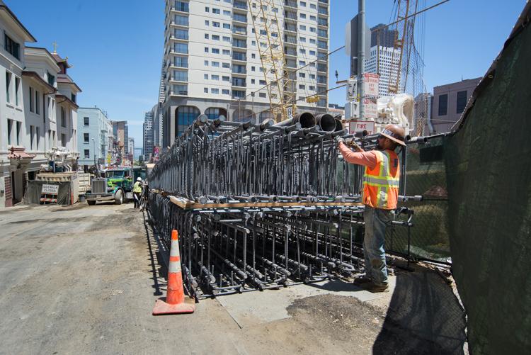 Worker in safety gear securing rebar cage on truck at Chinatown Station construction site.