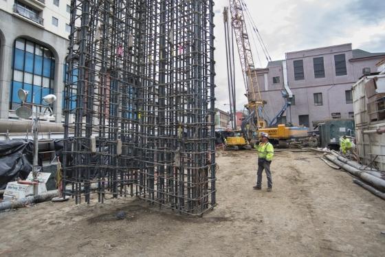 Construction site with steel rebar framework and heavy equipment at future Chinatown Station on Stockton Street.