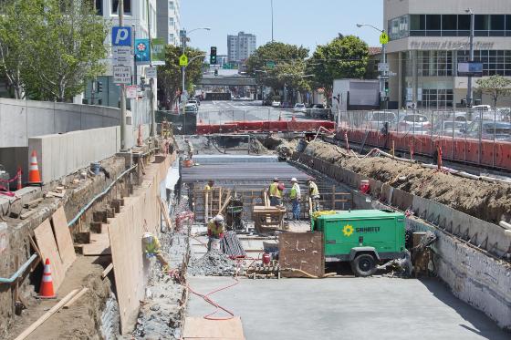 Construction site on 4th Street with concrete foundation work, equipment, and workers for future transit station.