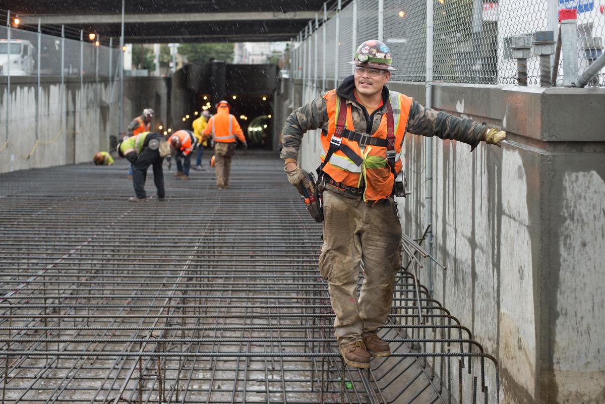 Construction worker in safety vest and hard hat on rebar framework at transit tunnel portal project site.