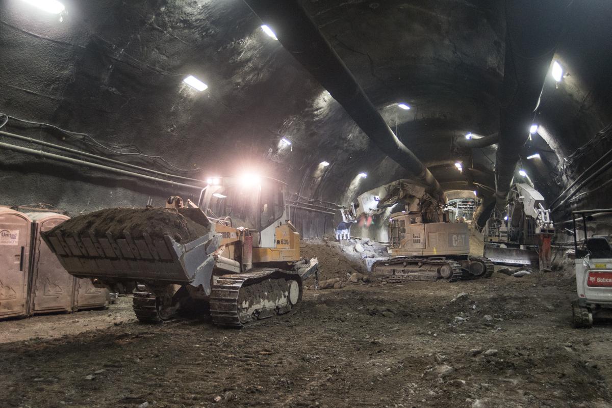 Underground tunnel excavation site with heavy equipment including bulldozer and excavator moving earth material.