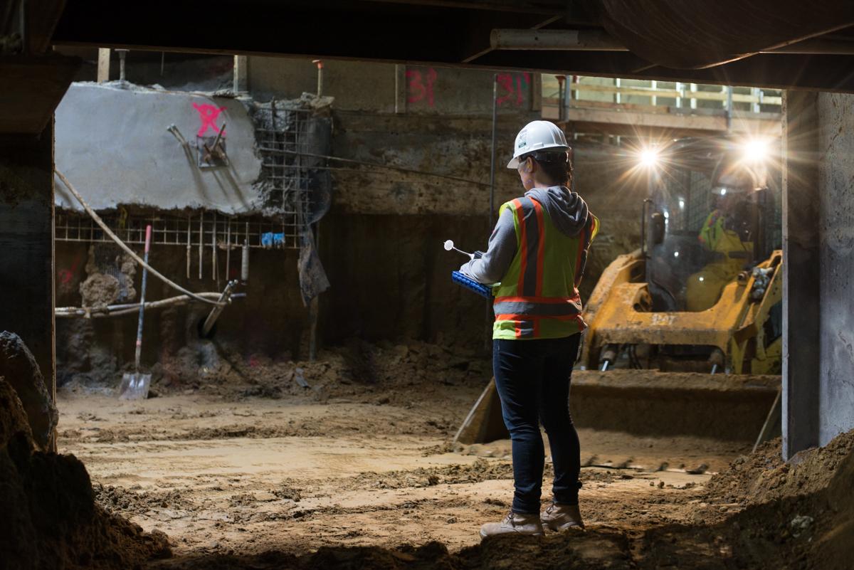 Construction worker in safety gear inspecting excavation work in underground station concourse.