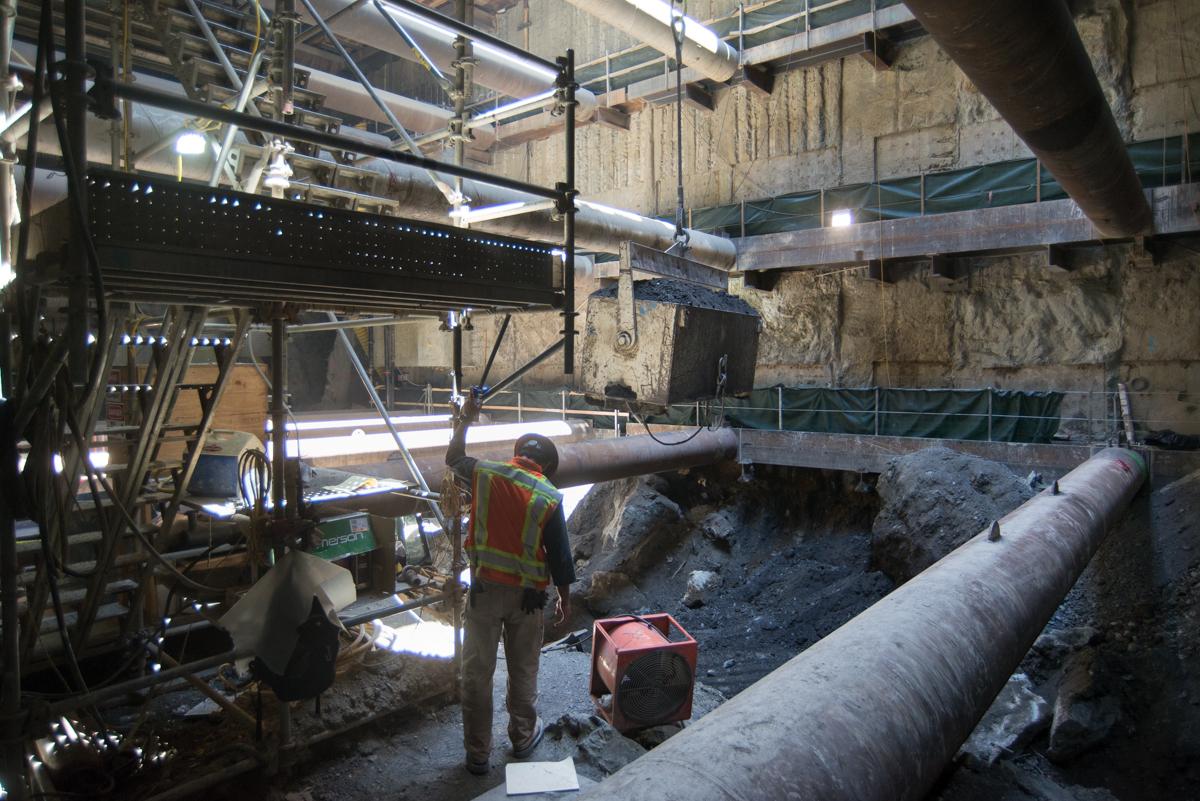 Worker in safety gear at underground construction site with large pipes and excavation equipment.