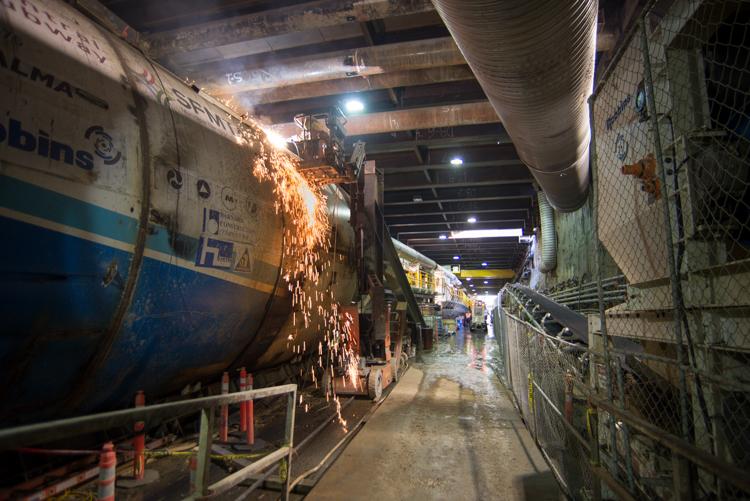 Welder performing maintenance on tunnel boring machine in underground transit construction site.