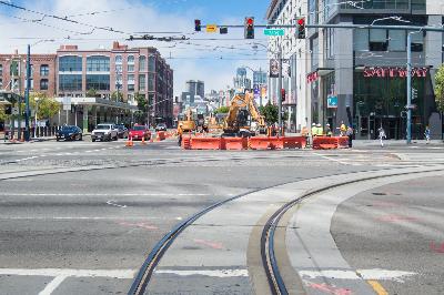 Street intersection with exposed rail lines, construction barriers, and utility work visible on urban street.