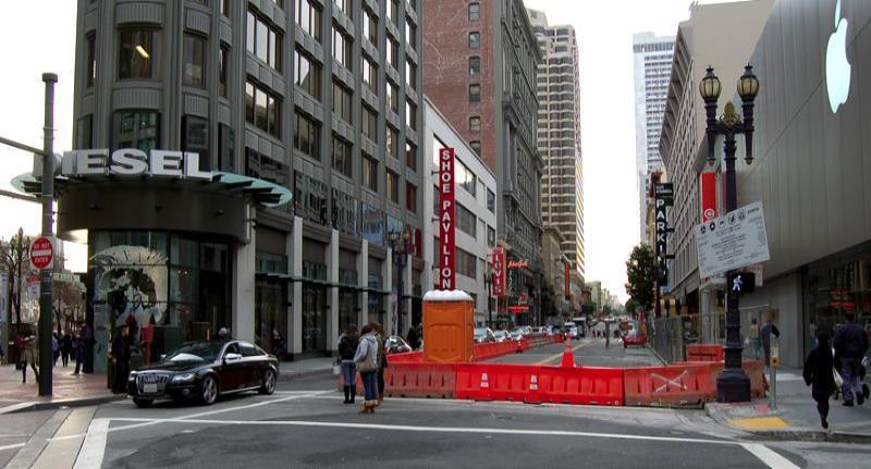 Ellis Street construction site with red barriers, pedestrians, and surrounding downtown buildings