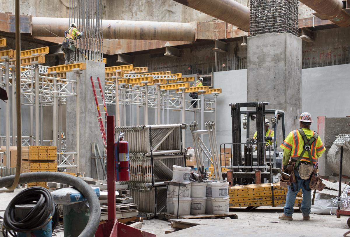 Construction worker in safety gear operating forklift inside concrete station structure with yellow scaffolding and metal framework.