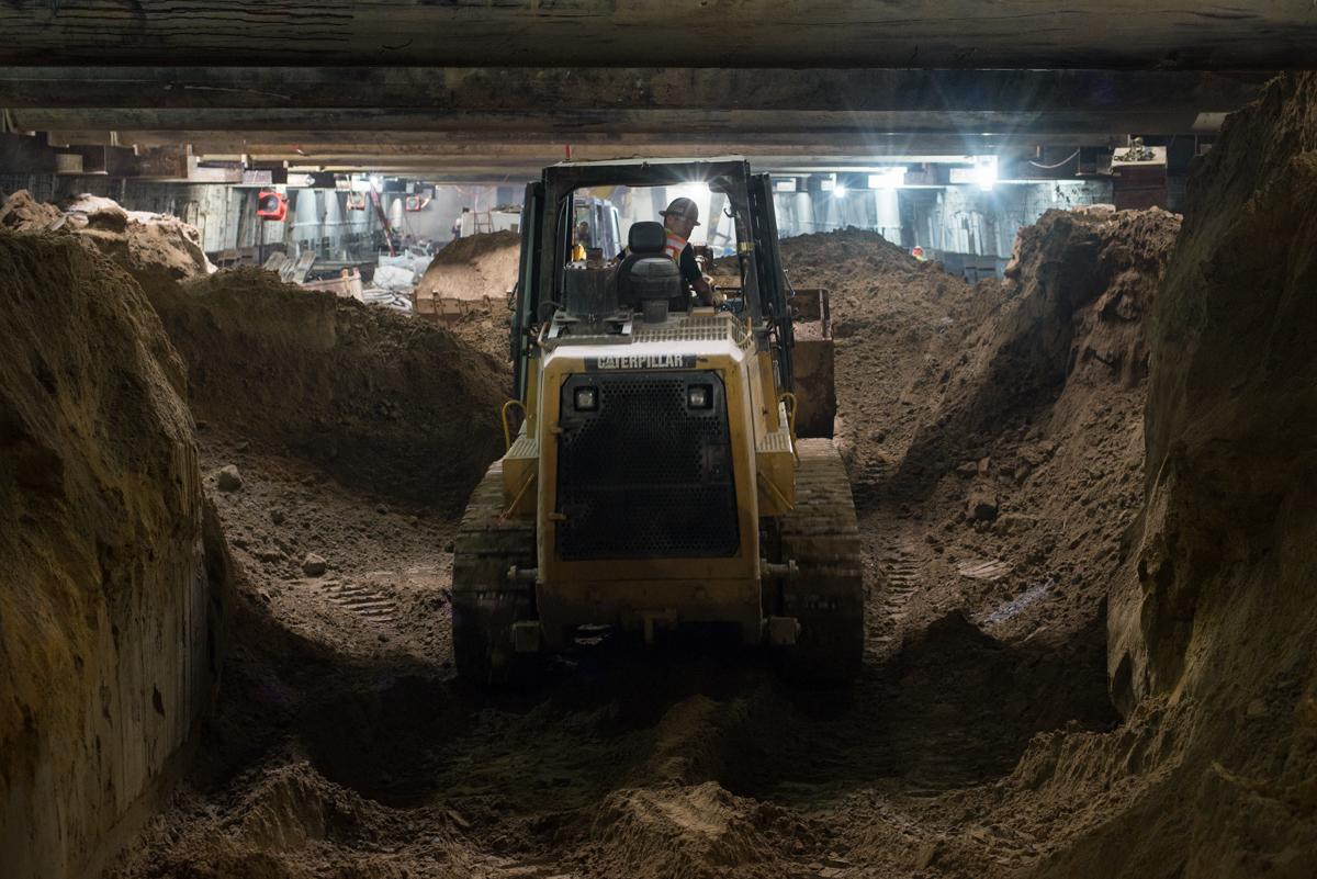 Bulldozer operating in underground construction trench beneath city street during transit station work.