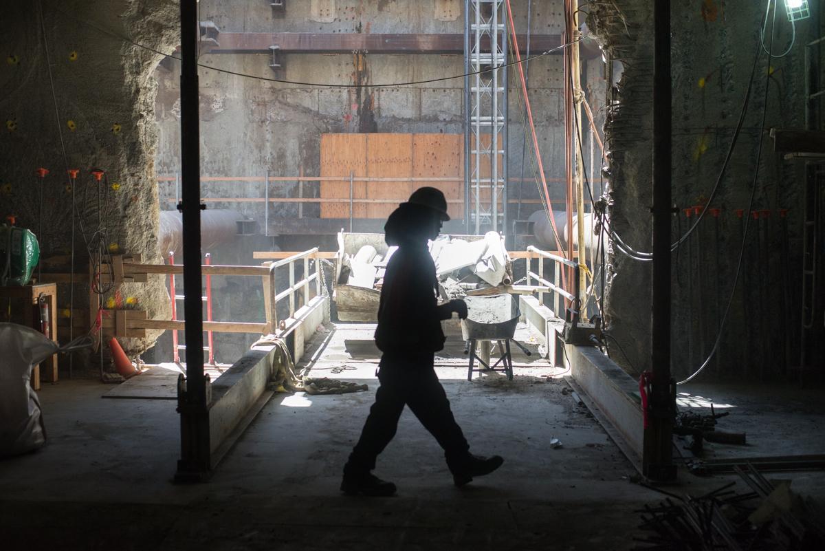 Worker in silhouette walking through construction site with excavation equipment and scaffolding visible beyond.