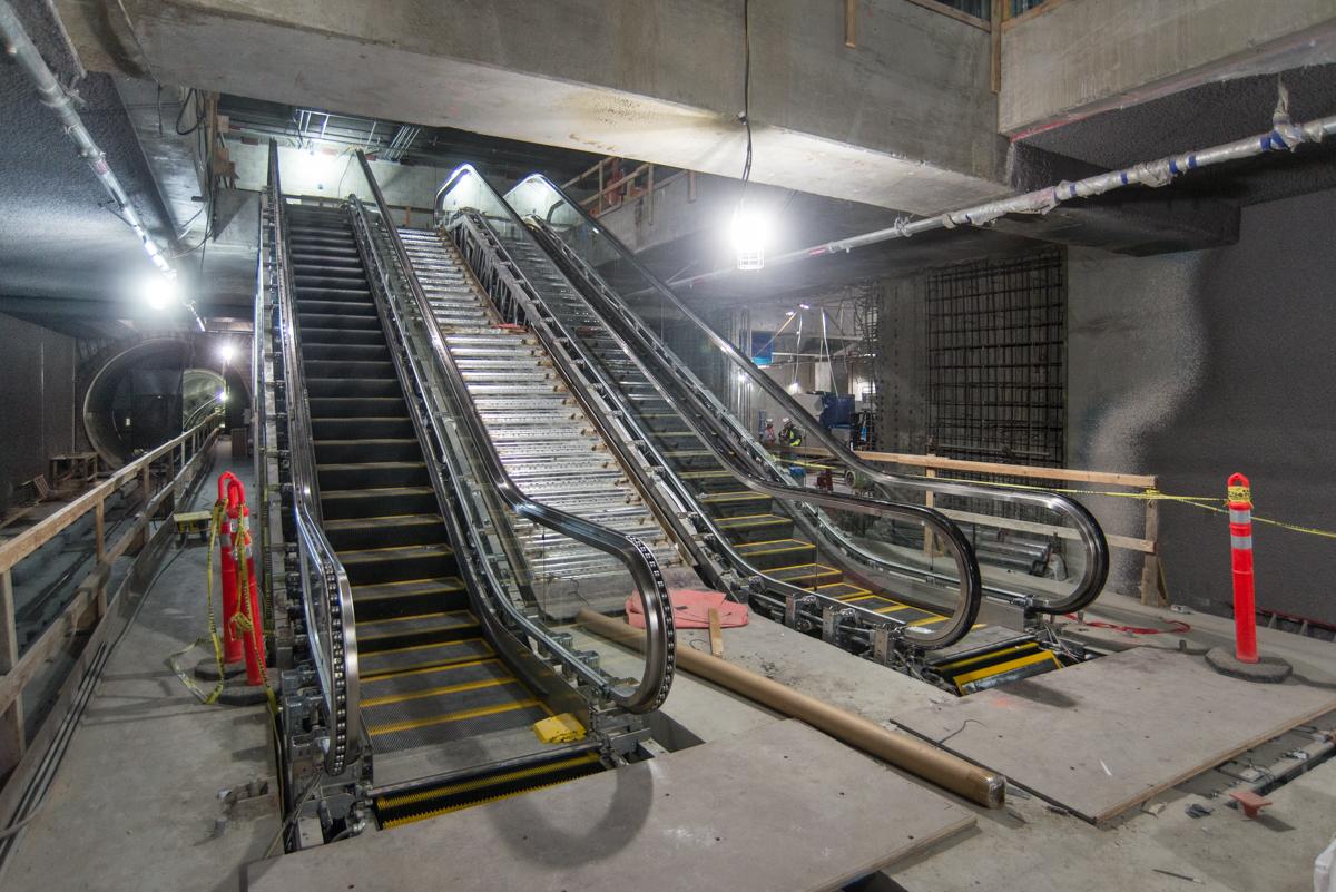 New escalators under construction at Yerba Buena/Moscone Station with handrails being installed.