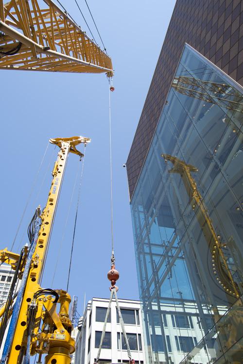 Construction cranes lifting materials above Stockton Street in downtown San Francisco with surrounding buildings.