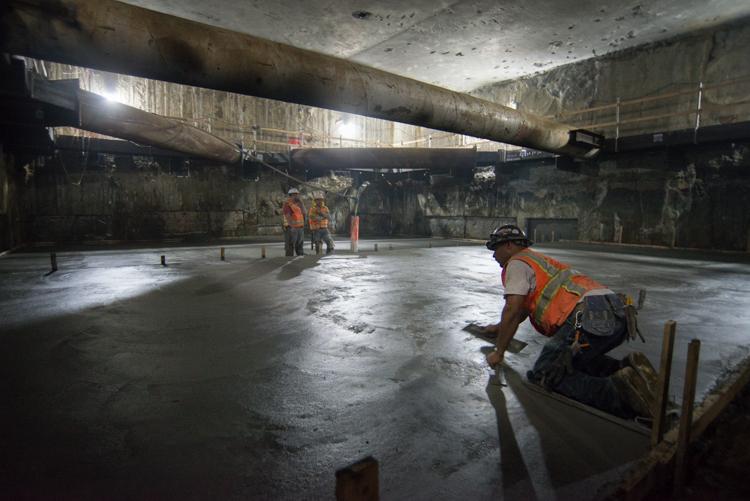 Workers in safety vests install steel reinforcing inside underground transit station during construction.