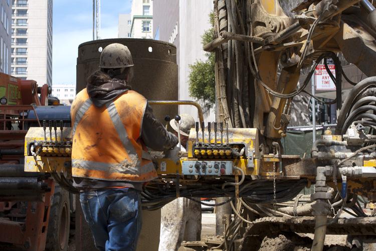 Construction worker in yellow safety vest operating drilling equipment on Stockton Street.