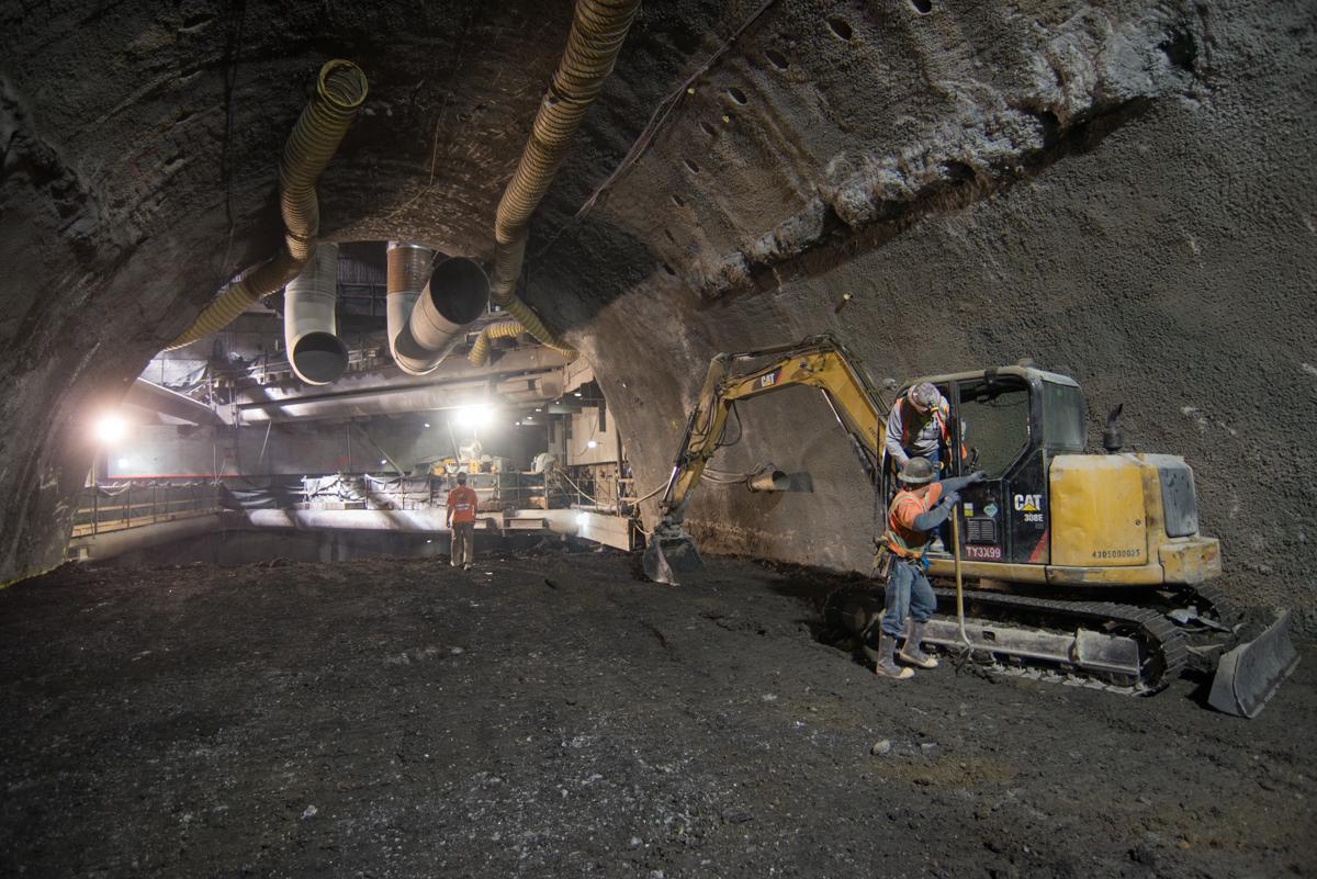 Underground tunnel construction site with yellow excavator, workers, and large pipes overhead at Stockton Street.