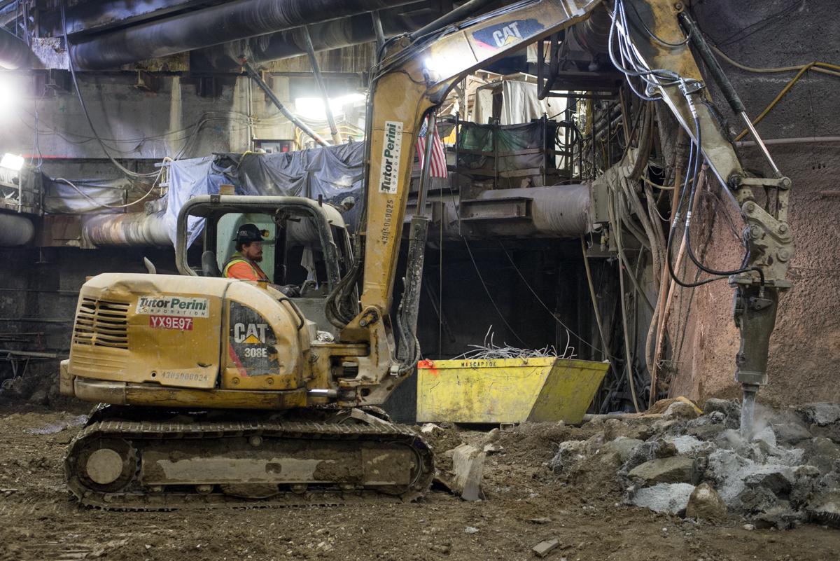 Excavator breaking down concrete debris from station platform cavern near construction headhouse at night.