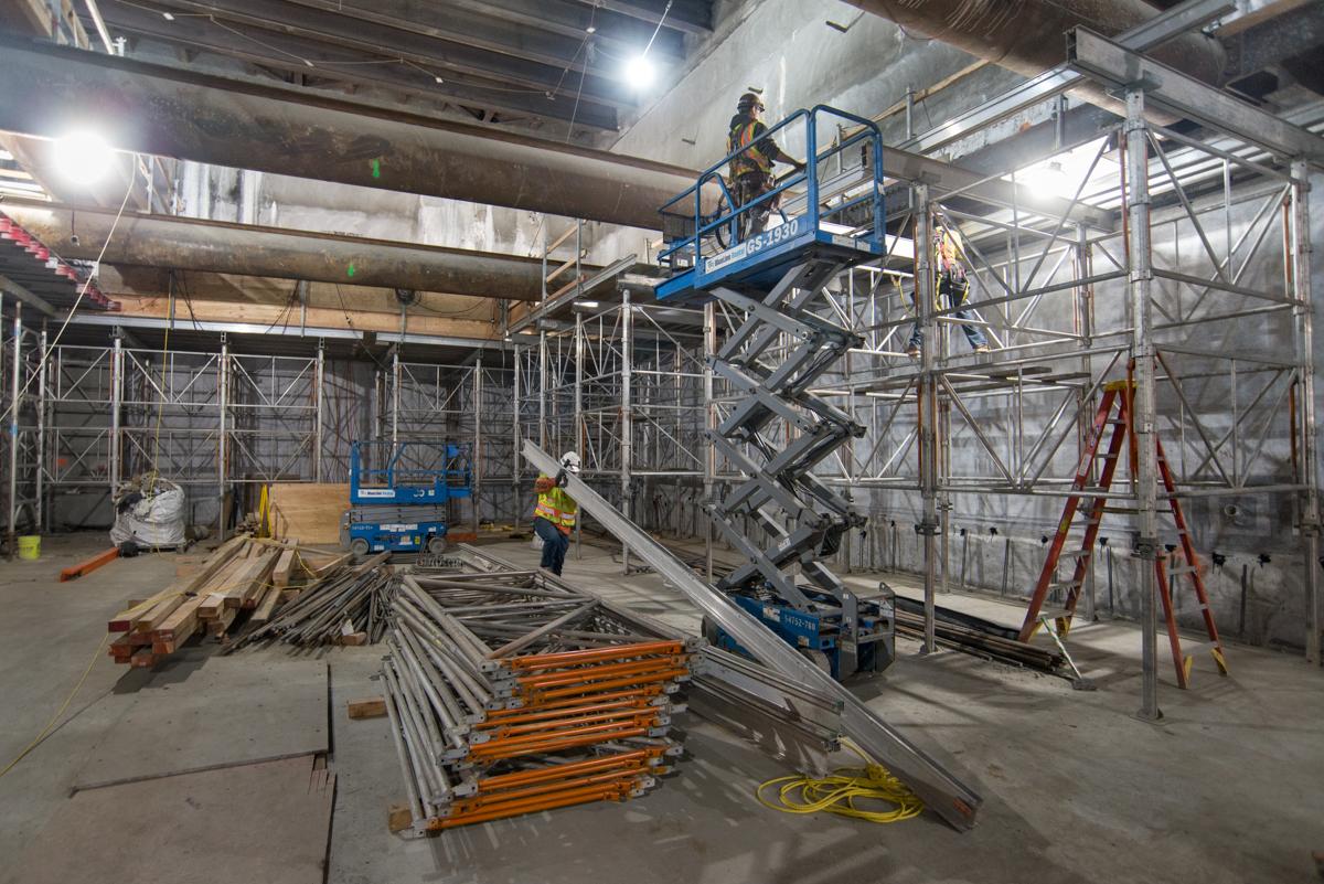 Construction workers on scissor lift assembling heavy-duty scaffolding in underground transit station with structural steel and materials.