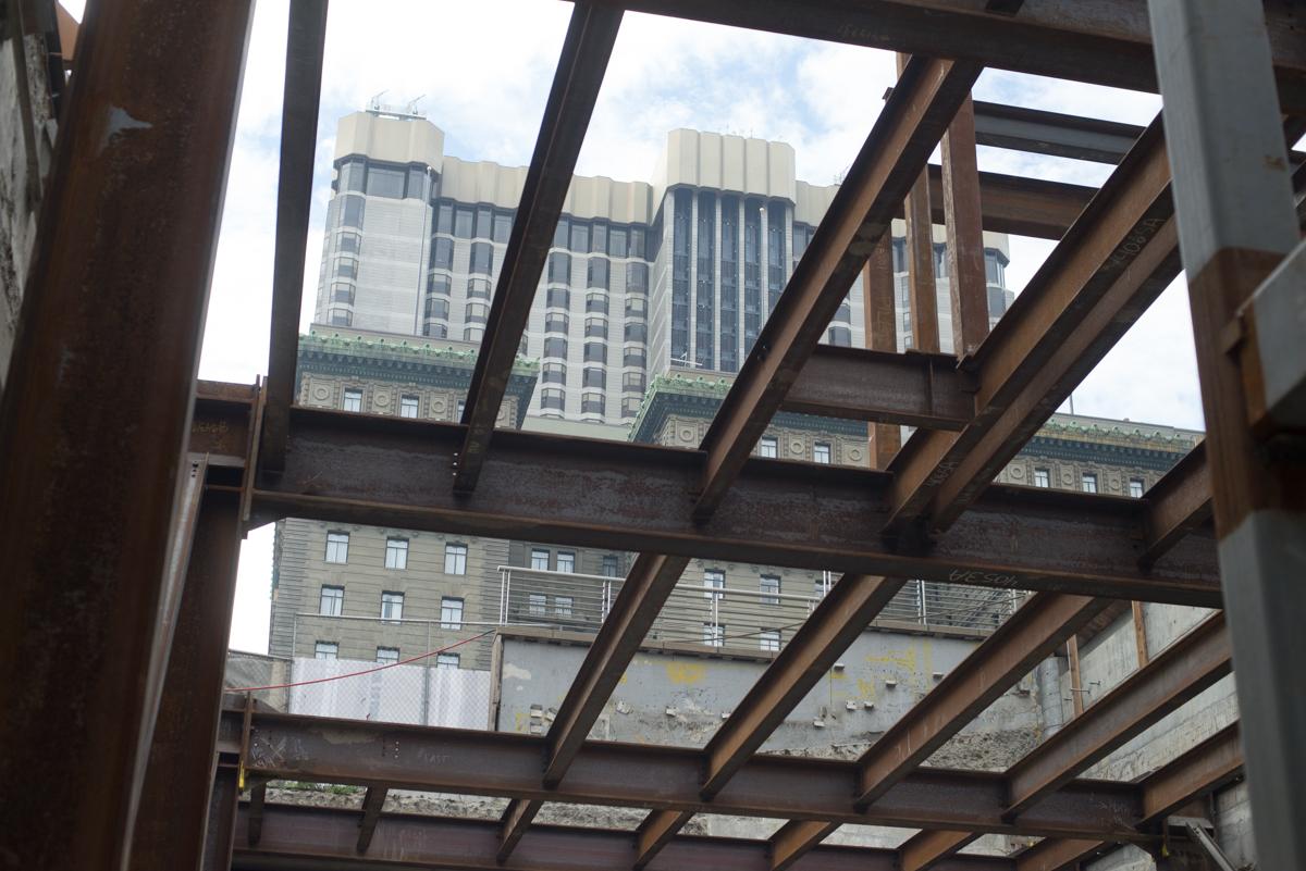 Steel framework structure under construction viewed from below, with San Francisco buildings visible above