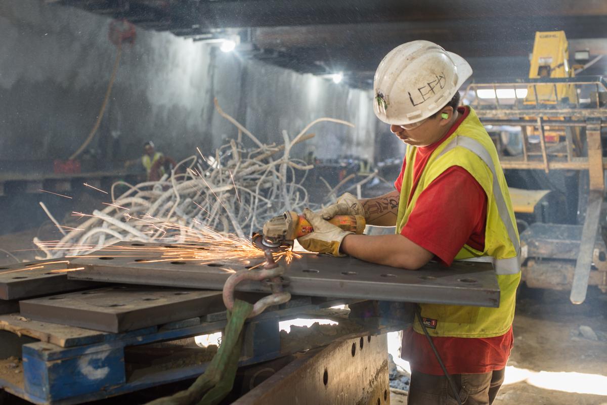 Worker in safety gear cutting steel bracket with angle grinder at construction site.
