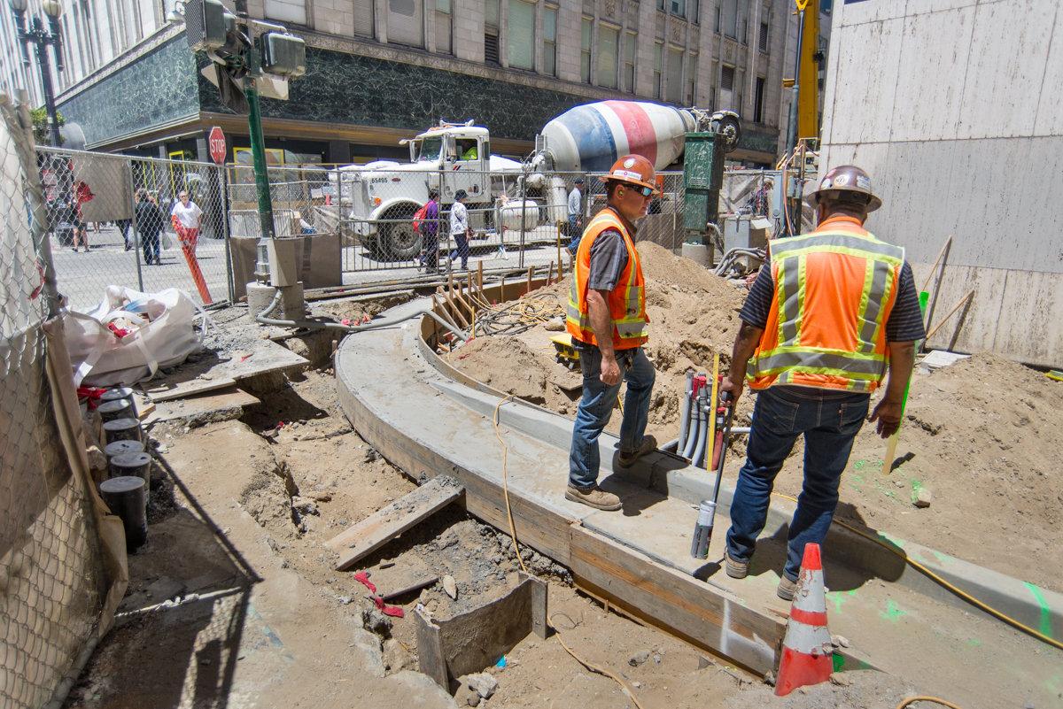 Construction workers install concrete curb at Stockton and O'Farrell Streets intersection.