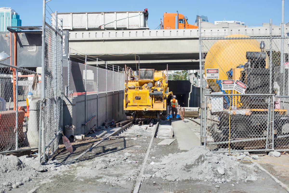 Yellow rail maintenance vehicle positioned at tunnel portal entrance with workers and equipment visible at construction site.