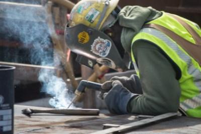 Worker in safety vest welding steel panels at transit station construction site