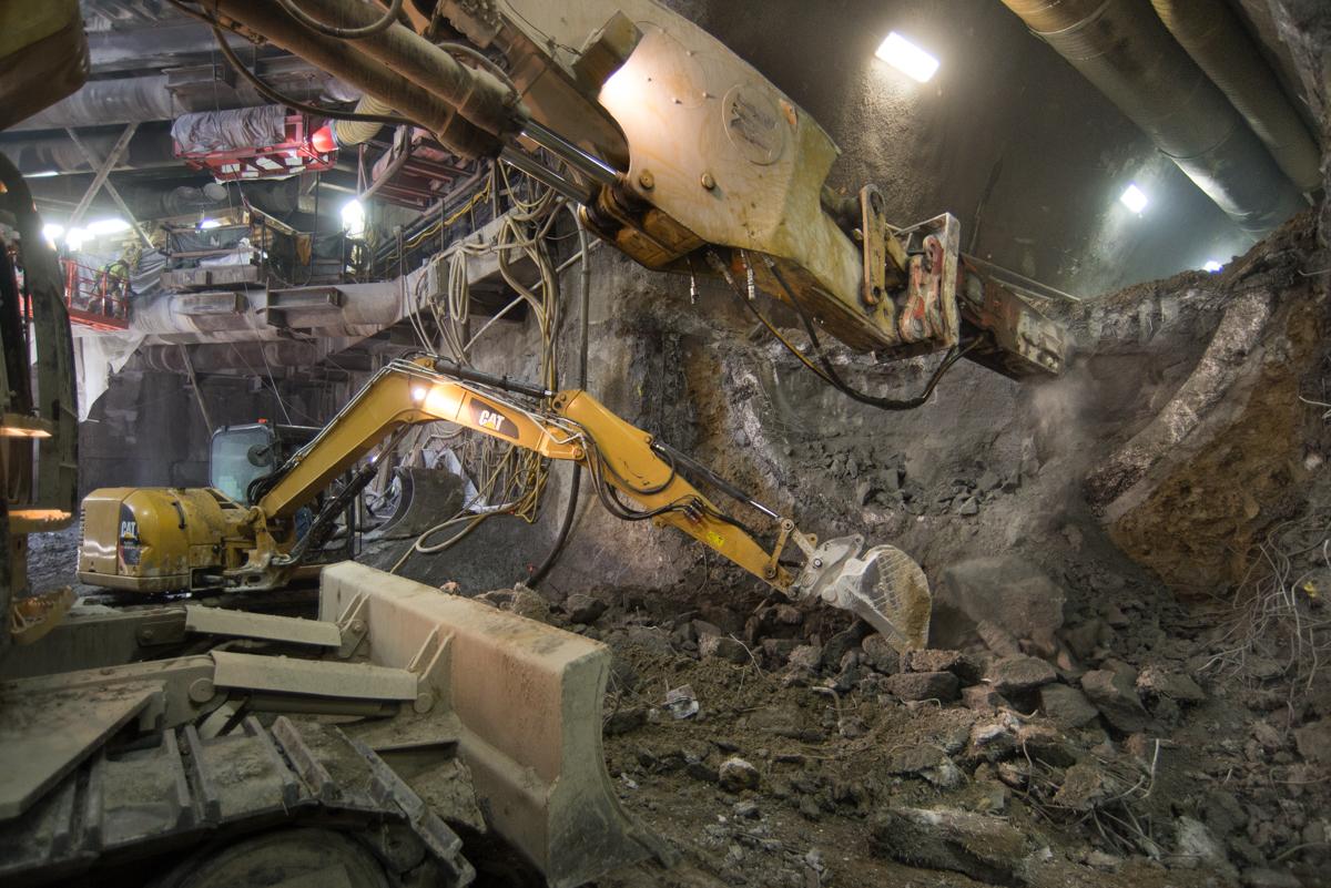 Underground tunnel excavation with two yellow excavators breaking concrete at night.