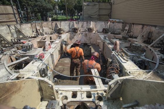 Workers disassemble tunnel boring machine shield section in underground pit.