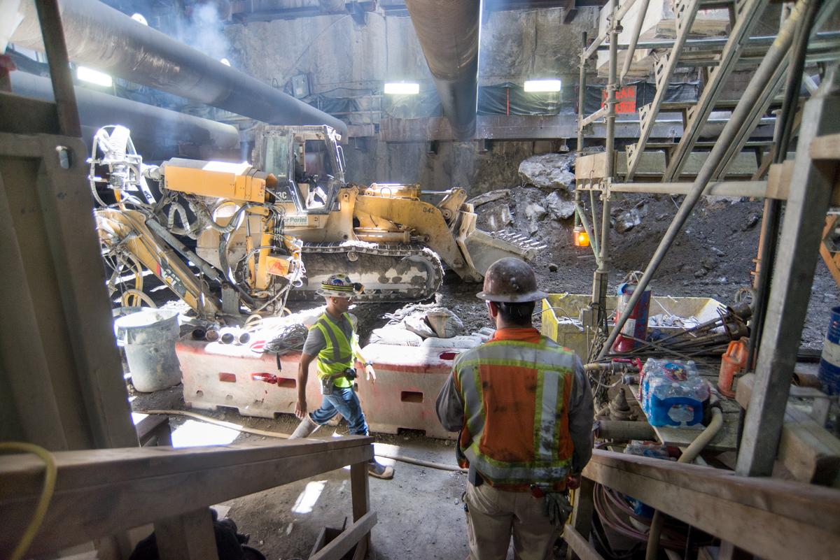 Workers in safety gear operate heavy equipment including a bulldozer in an underground transit construction site at night.