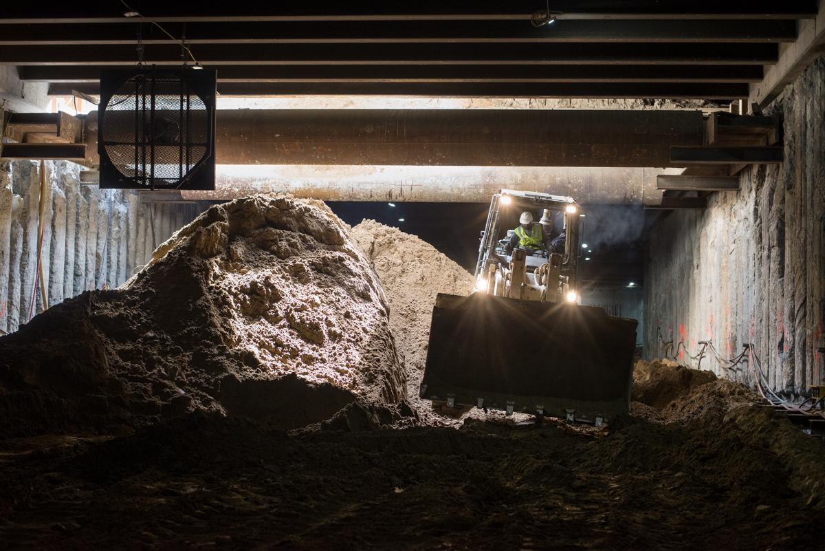 Bulldozer moving excavated soil inside underground station box during construction work.