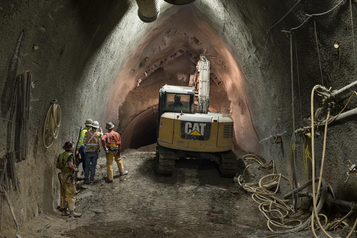 Workers and CAT excavator inside underground tunnel during sewer excavation project.
