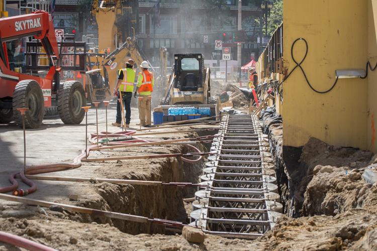 Construction crew working on underground utility removal with reinforced subsurface forms and heavy equipment on urban street.