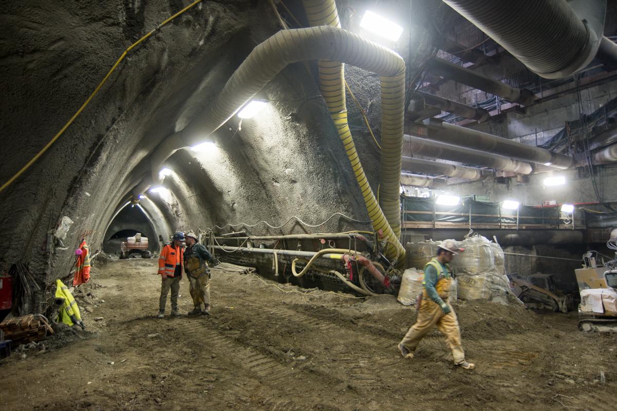 Workers in safety gear inside a large underground tunnel with ventilation ducts and construction equipment.
