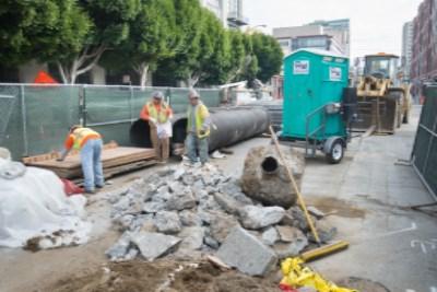 Construction crew excavating and sorting materials around underground utilities on urban street.