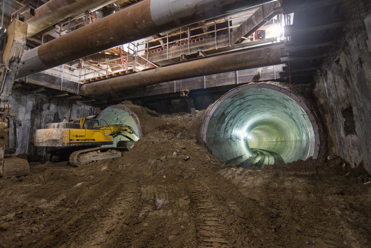 Excavator removing tunnel lining segments from underground station box construction site.