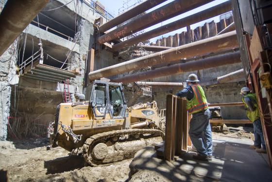 Construction workers guide a bulldozer moving steel beams inside Yerba Buena Moscone Station headhouse.